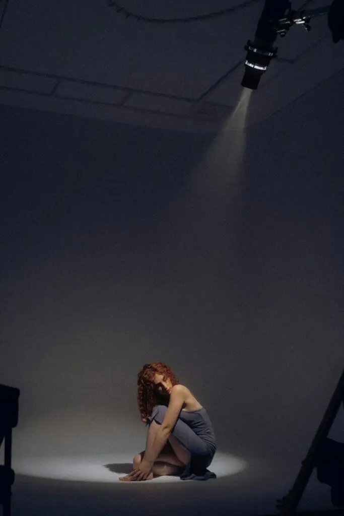 Actriz sentada bajo un foco de estudio, en un momento de introspección y exposición emocional